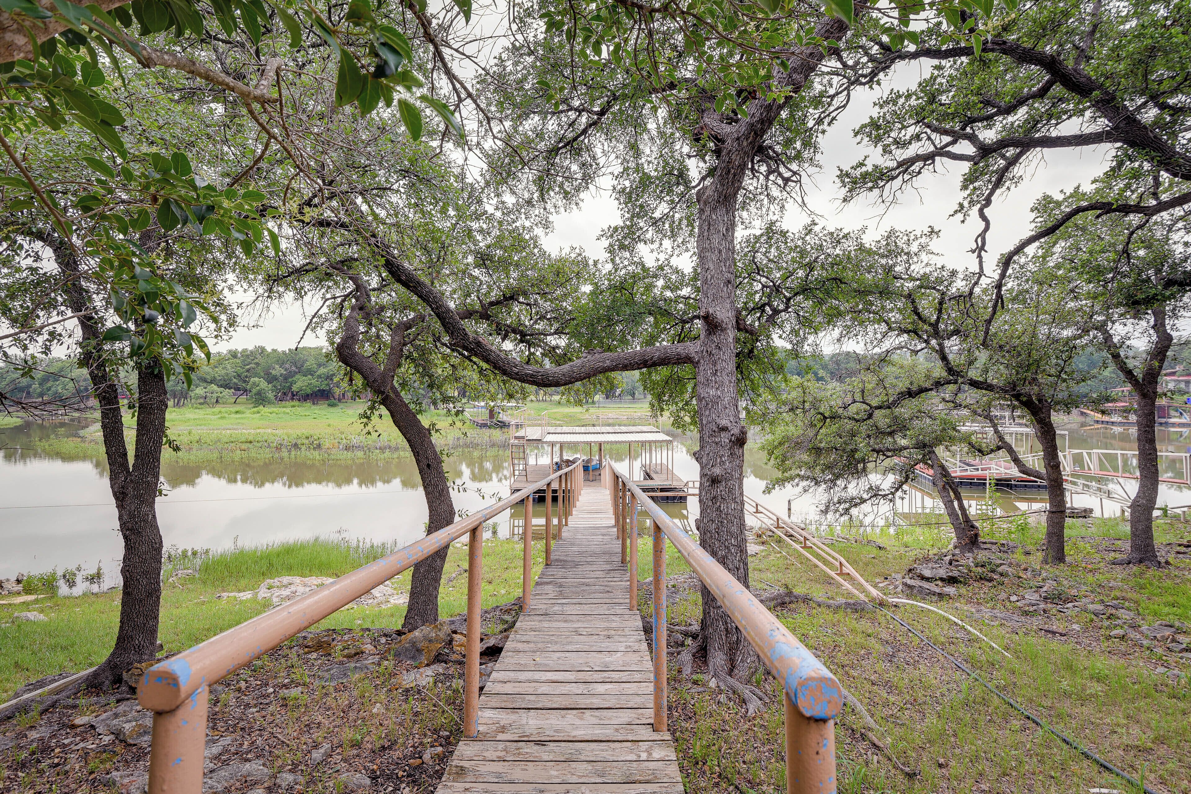 Un pont en bois menant à une jetée surplombant un lac paisible, entouré d’arbres et de zones herbeuses.