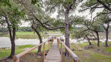 A wooden bridge leading to a dock over a calm lake, surrounded by trees and grassy areas.