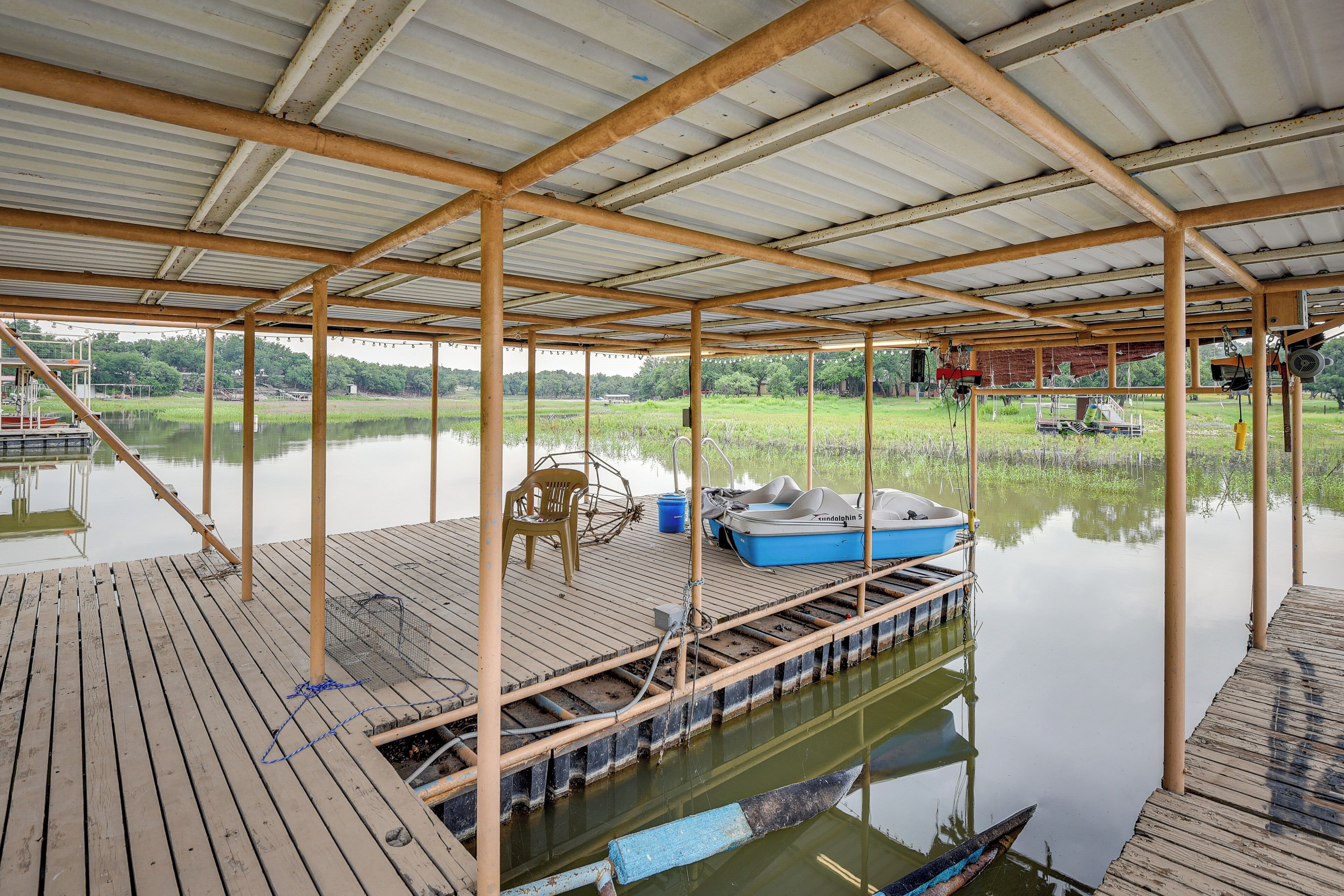 Un muelle de madera cubierto con un bote, una silla y un cubo azul.