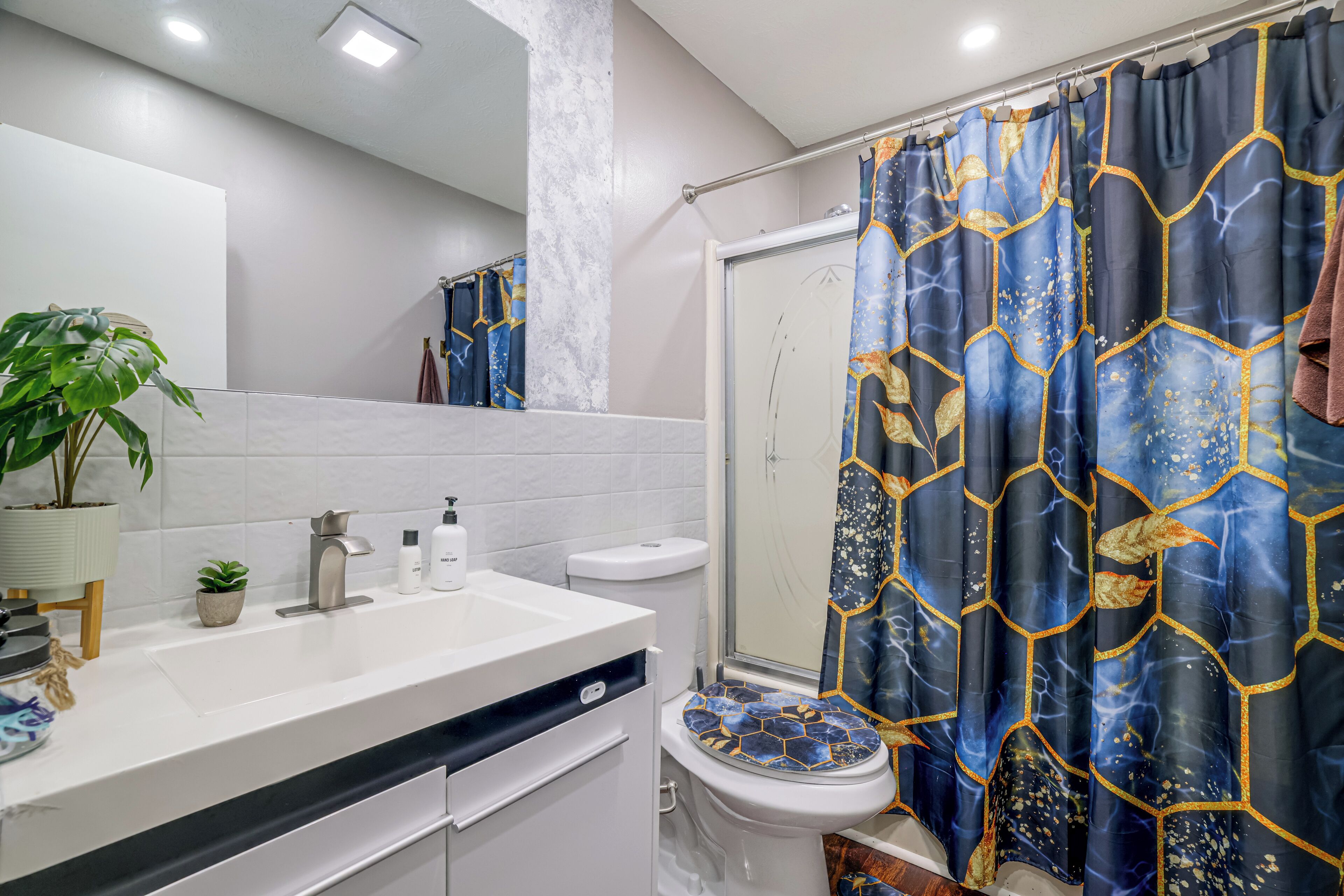 A bathroom with a white sink, a toilet, a shower curtain with a geometric pattern, and a potted plant.