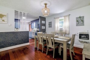 Un coin repas avec une table et des chaises en bois, un lustre et une vue sur la cuisine.