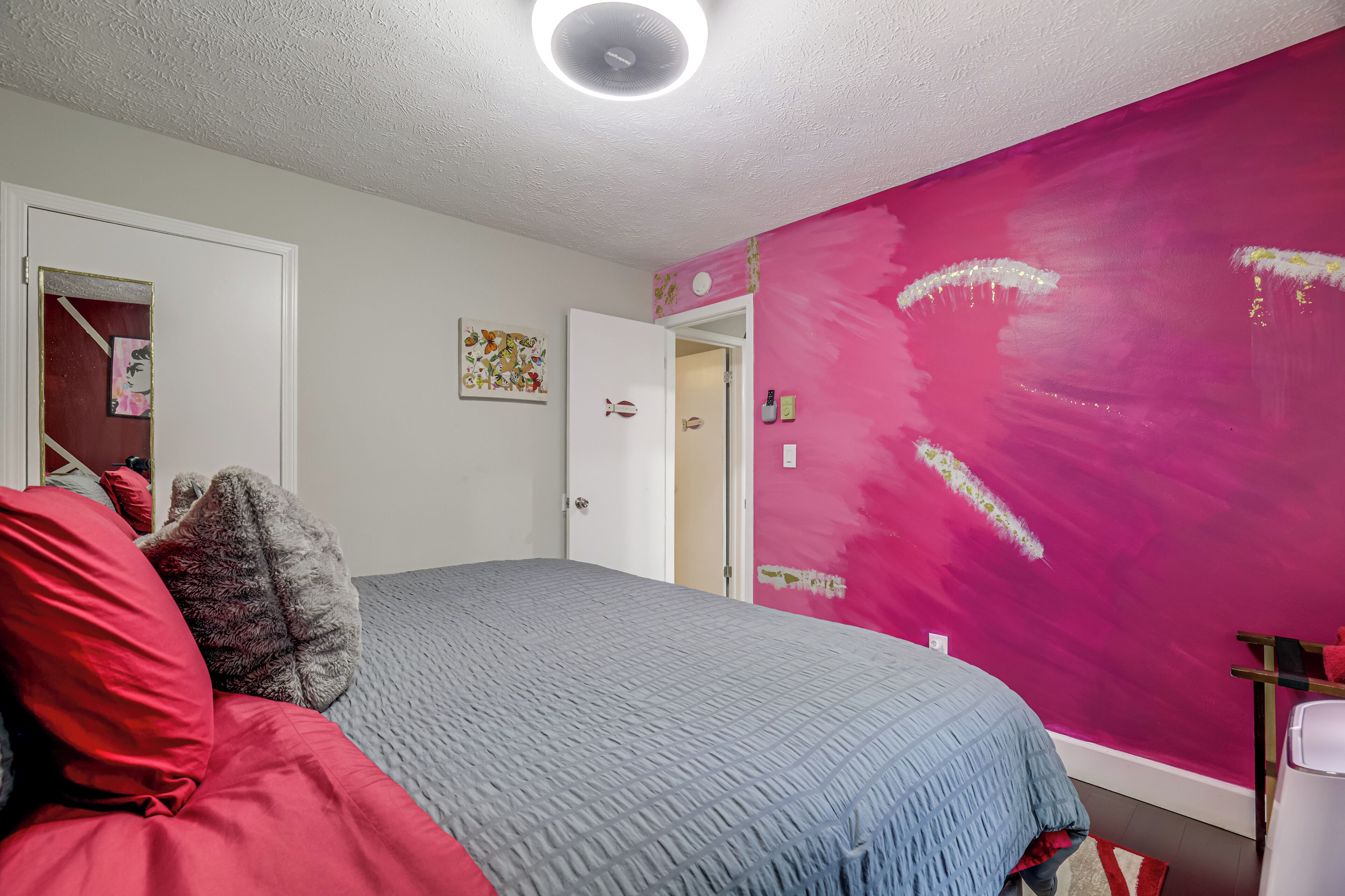 A bedroom with a bed, a door, and a wall with a pink paint job.