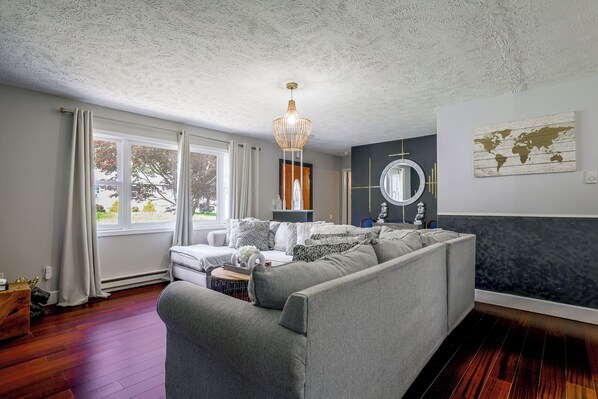 A modern living room with a grey sectional sofa, a round mirror, and a world map artwork on the wall. - 'A Time to Remember' Home in Tobyhanna w/ hot tub (Tobyhanna)
