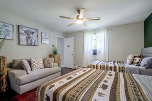 Una habitación de hotel con cama, sofá, ventilador de techo y ventana con cortinas.