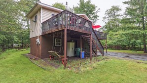 Une maison à deux étages dotée d’une terrasse en bois et d’un escalier menant à un balcon situé au deuxième étage.