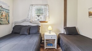 Une chambre avec deux lits, une table de chevet avec une lampe, une fenêtre avec des rideaux et un tableau au mur.
