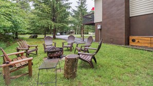 Un espace extérieur aménagé avec des chaises en bois et une table en métal, entouré de pelouse et d’arbres, avec un bâtiment en arrière-plan.