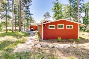 A red cabin with a porch, surrounded by trees and a clear sky. - Waterfront Pequot Lakes Cabin: Fire Pit + Views! (Pequot Lakes)