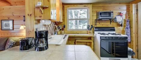 A wooden cabin kitchen with a stove, microwave, and coffee maker.