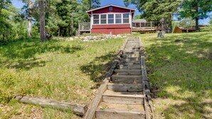 A red cabin with a wooden deck and a staircase leading to a covered area. - Waterfront Pequot Lakes Cabin: Fire Pit + Views! (Pequot Lakes)