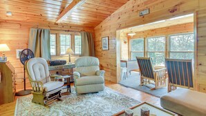 A cozy cabin interior with wooden walls, a large window, a fan, a desk, a chair, and a couch. - Waterfront Pequot Lakes Cabin: Fire Pit + Views! (Pequot Lakes)