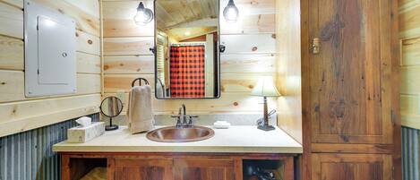 Une salle de bain rustique, aménagée dans une cabane en bois, avec un lavabo, un miroir, une serviette et un meuble de rangement.