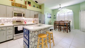 A kitchen with white cabinets, a microwave, and a refrigerator. There is a dining area with a table and chairs. - Lanai & Grill: Sunny Home Near Rainbow Springs! (Dunnellon)