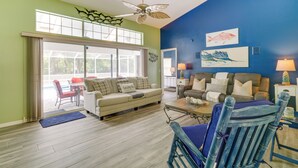 A living room with a sofa, coffee table, and chairs, a ceiling fan, and artwork on the walls. - Lanai & Grill: Sunny Home Near Rainbow Springs! (Dunnellon)