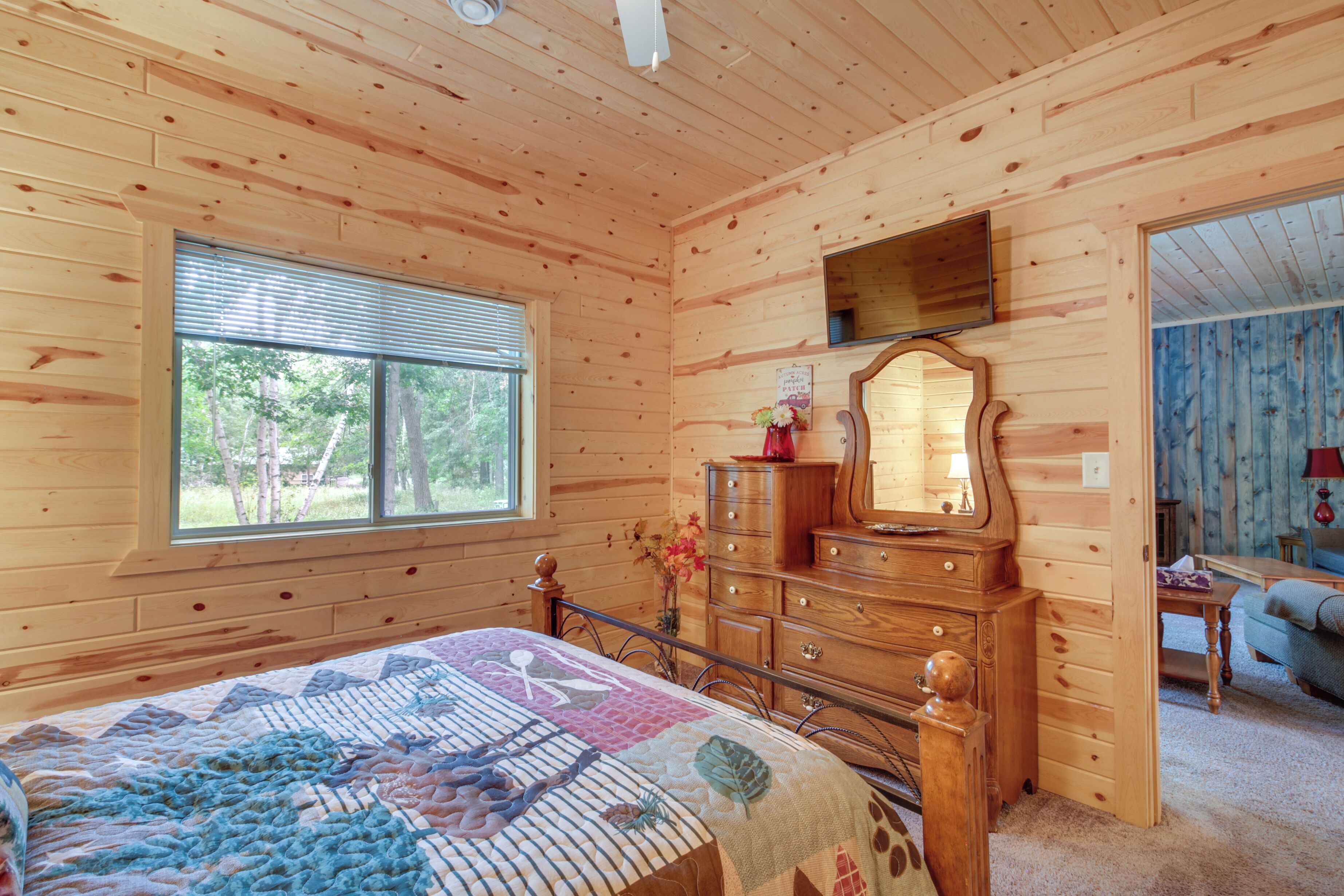 Ein Schlafzimmer in einer Holzhütte mit Bett, Kommode, Spiegel und Fenster.