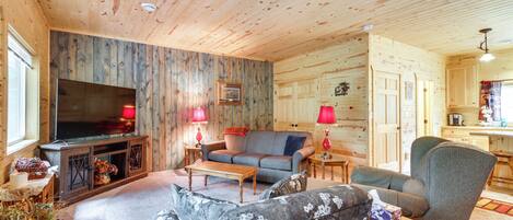 A cozy log cabin interior with a living room featuring a sofa, armchair, and a television.