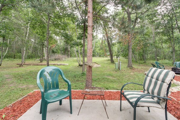 An outdoor patio area with two chairs and a small table, surrounded by trees and a grassy lawn.