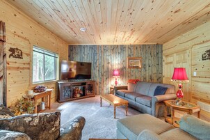L’intérieur d’un chalet accueillant, avec un plafond en bois, un téléviseur, un canapé, une table basse et une cheminée.