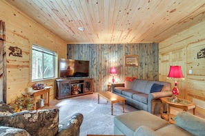 A cozy cabin interior with a wooden ceiling, a television, a sofa, a coffee table, and a fireplace.