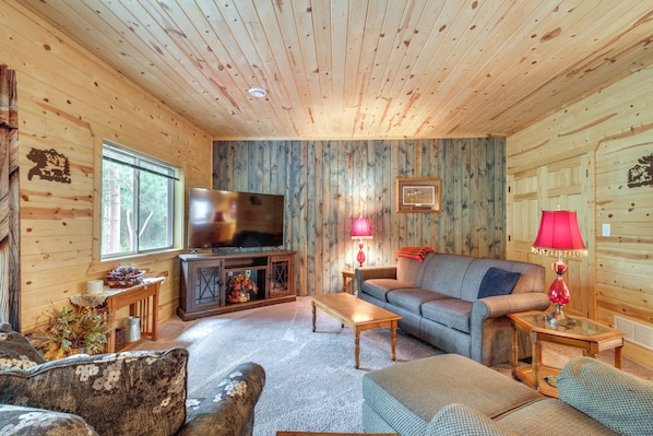 A cozy cabin interior with a wooden ceiling, a television, a sofa, a coffee table, and a fireplace. - Pequot Lakes Vacation Rental w/ Patio & Fire Pit (Pequot Lakes)