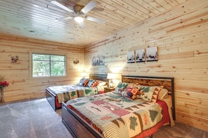 A log cabin bedroom with two beds, a ceiling fan, and a large window.