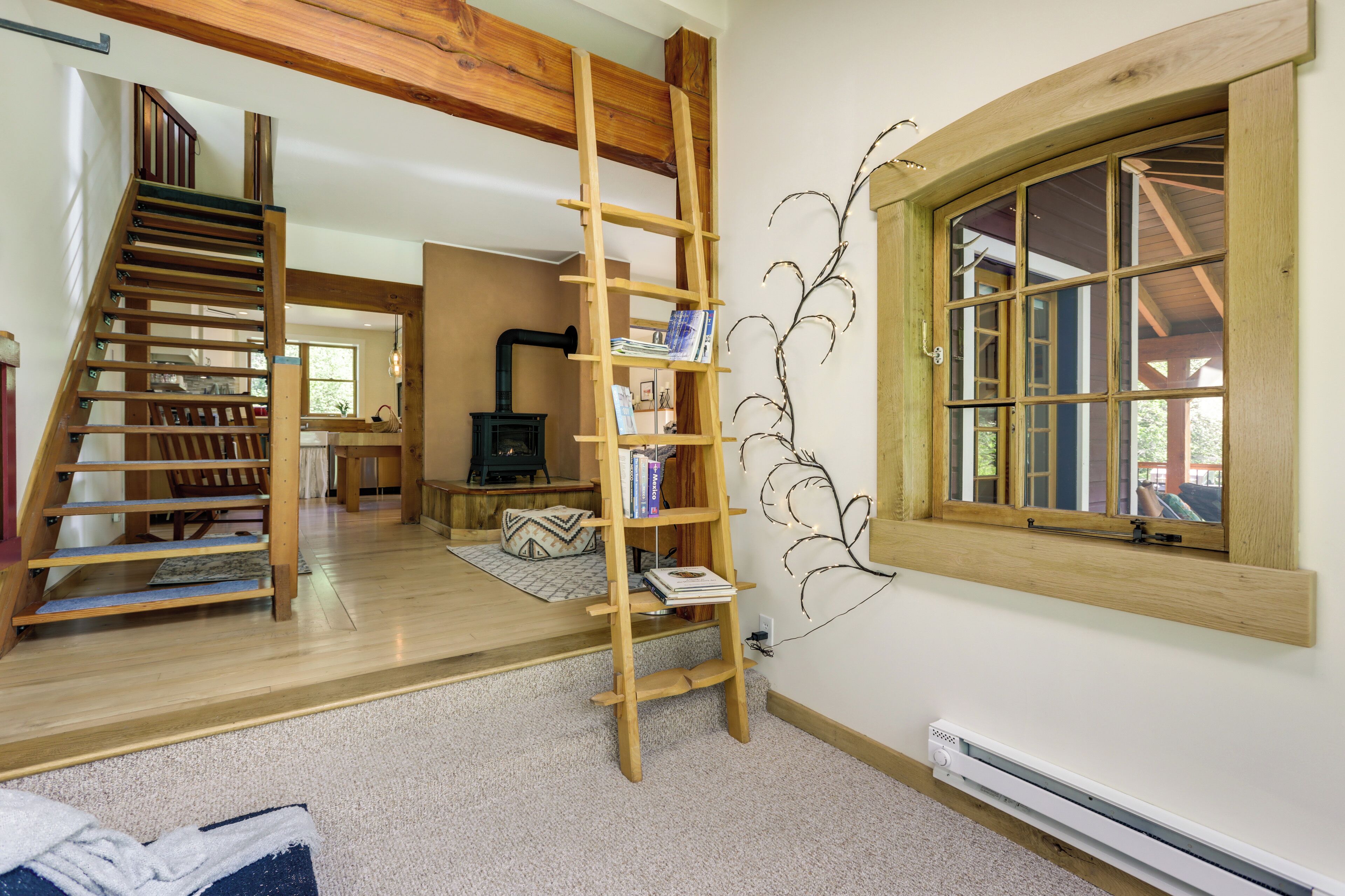 A spacious living area with a wooden staircase, a ladder, a fireplace, and a large window.