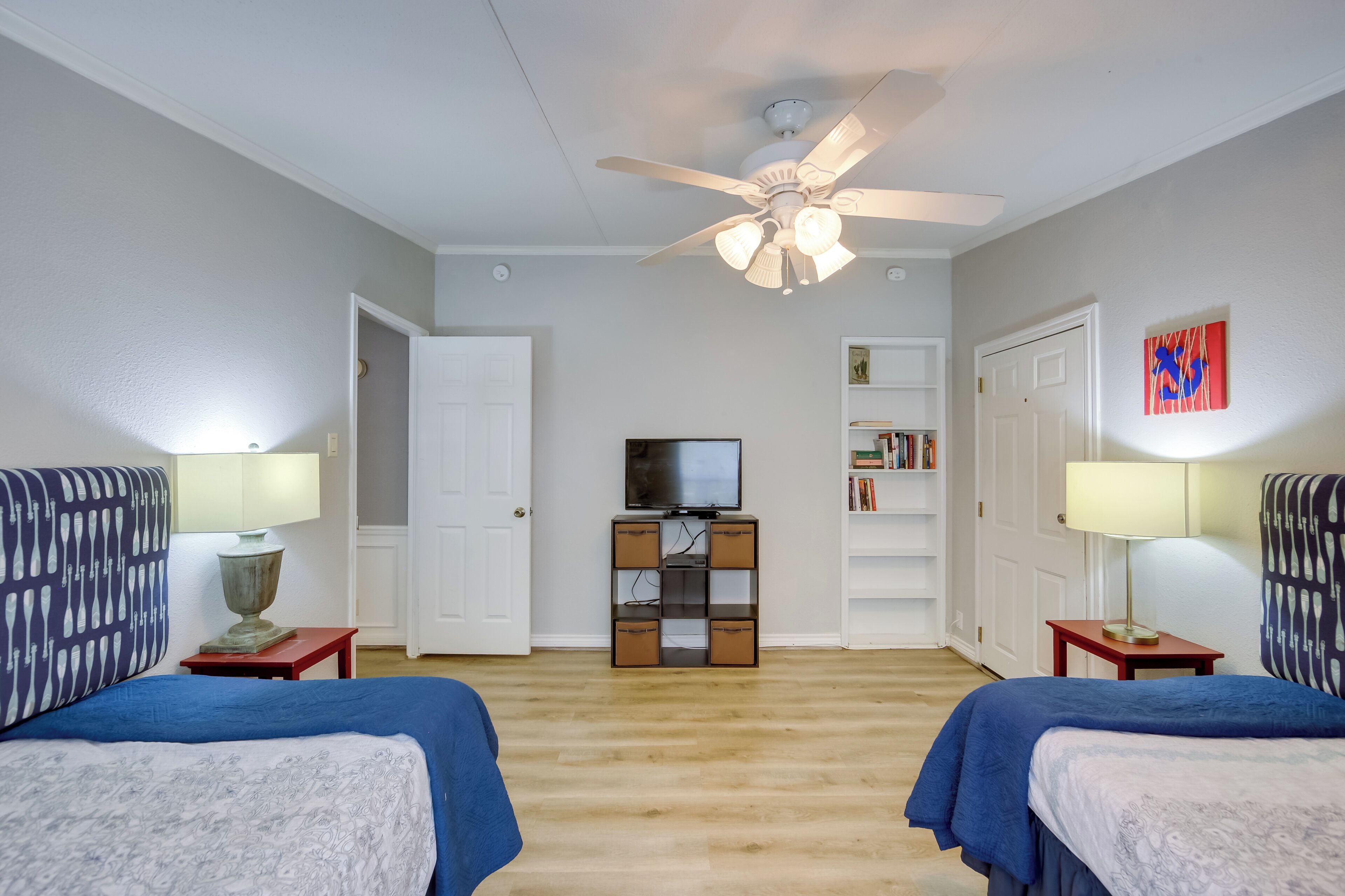 A bedroom with two beds, a ceiling fan, a TV, and a bookshelf.