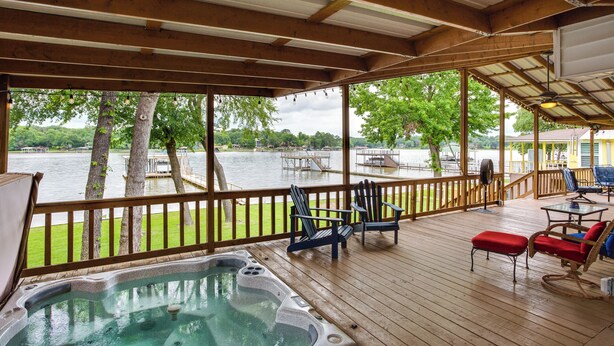 Una terrazza in legno con idromassaggio, sedie e vista su un lago.
