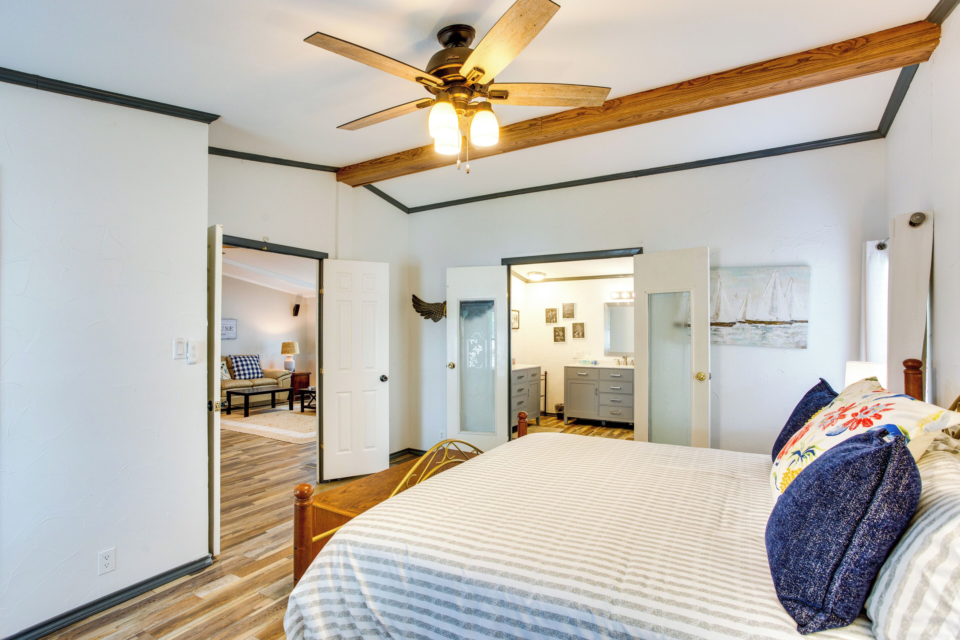 A bedroom with a bed, wooden ceiling beams, a ceiling fan, and a door leading to another room.