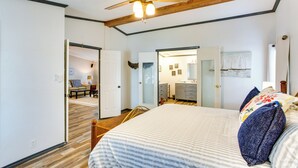 Una camera da letto con un letto, travi in legno a soffitto, una ventola a soffitto e una porta che dà su un'altra stanza.