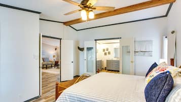 A bedroom with a bed, wooden ceiling beams, a ceiling fan, and a door leading to another room.