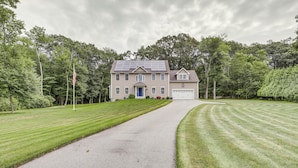 A two-story house with a driveway leading to a garage, surrounded by well-maintained lawns and trees. - Spacious Connecticut Home - Deck, Grill & Fire Pit (Mystic)