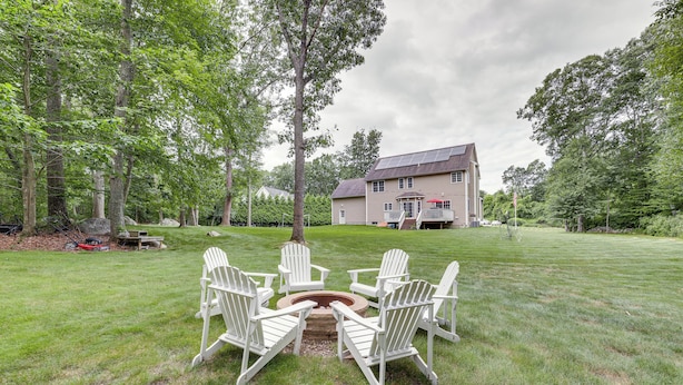 A large house with a lawn, a fire pit, and several Adirondack chairs arranged around it. - Spacious Connecticut Home - Deck, Grill & Fire Pit (Mystic)
