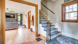 A spacious hallway with a wooden floor, a staircase with a metal railing, and a kitchen area in the background. - Central Erie Vacation Rental ~ 2 Mi to Beach! (Erie)