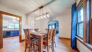 A dining area with a wooden table set for six, surrounded by chairs. A chandelier hangs above, and a sign on the wall reads "Everyone has a story." - Central Erie Vacation Rental ~ 2 Mi to Beach! (Erie)