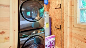 Un área de lavandería compacta con lavadora y secadora Samsung, un calentador de agua y un ventilador.