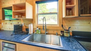 Una cocina con armarios de madera, un lavamanos de acero inoxidable y una ventana con vistas a la vegetación.