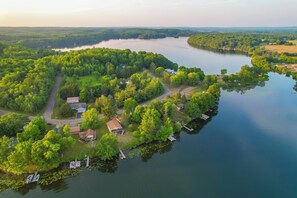 An aerial view of a lakeside property with a dock, boats, and houses surrounded by dense greenery.
