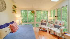 Una habitación con cama, dos sillones y amplias ventanas que dan a vistas de follaje.