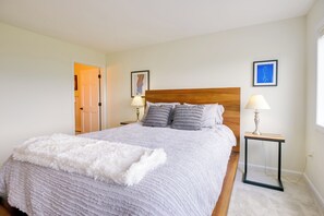 Ein ordentlich eingerichtetes Schlafzimmer mit einem großen Bett, zwei Nachttischen mit Lampen und einer Tür zu einem weiteren Raum.