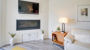 Un salon avec un téléviseur à écran plat fixé au-dessus d’une cheminée, un canapé, une table d’appoint avec une lampe et deux plantes en pot.