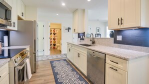 Une cuisine moderne avec des meubles blancs, des appareils en acier inoxydable et un tapis à motifs.