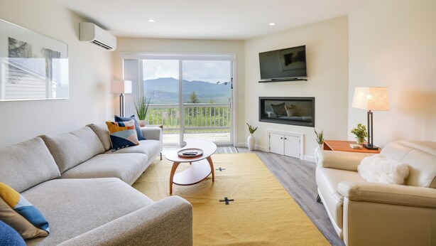 Un salon moderne avec un canapé, une table basse, un téléviseur et un balcon offrant une vue sur les montagnes.