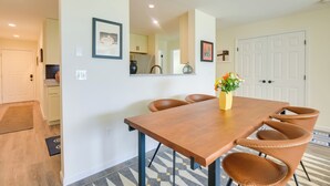 Un coin repas avec une table en bois et des chaises en cuir, un vase rempli de fleurs et, au fond, une cuisine.