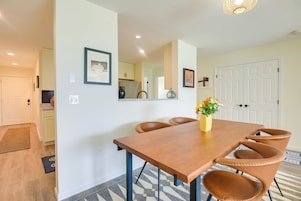 Comedor con mesa de madera y sillas de cuero, un jarrón con flores y una cocina al fondo.