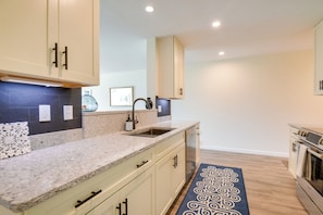 A modern kitchen with beige cabinets, a granite countertop, a stainless steel sink, and a patterned rug. - Newly Renovated Bartlett Condo w/ Mountain Views! (Intervale)