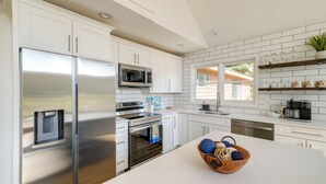Een moderne keuken met witte kasten, roestvrijstalen apparatuur en een groot eiland met een schaal fruit en groenten.