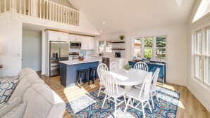 Een ruime woonkamer met een hoge plafond, een eettafel met stoelen, een keuken met witte kasten en een balkon met een hekwerk.