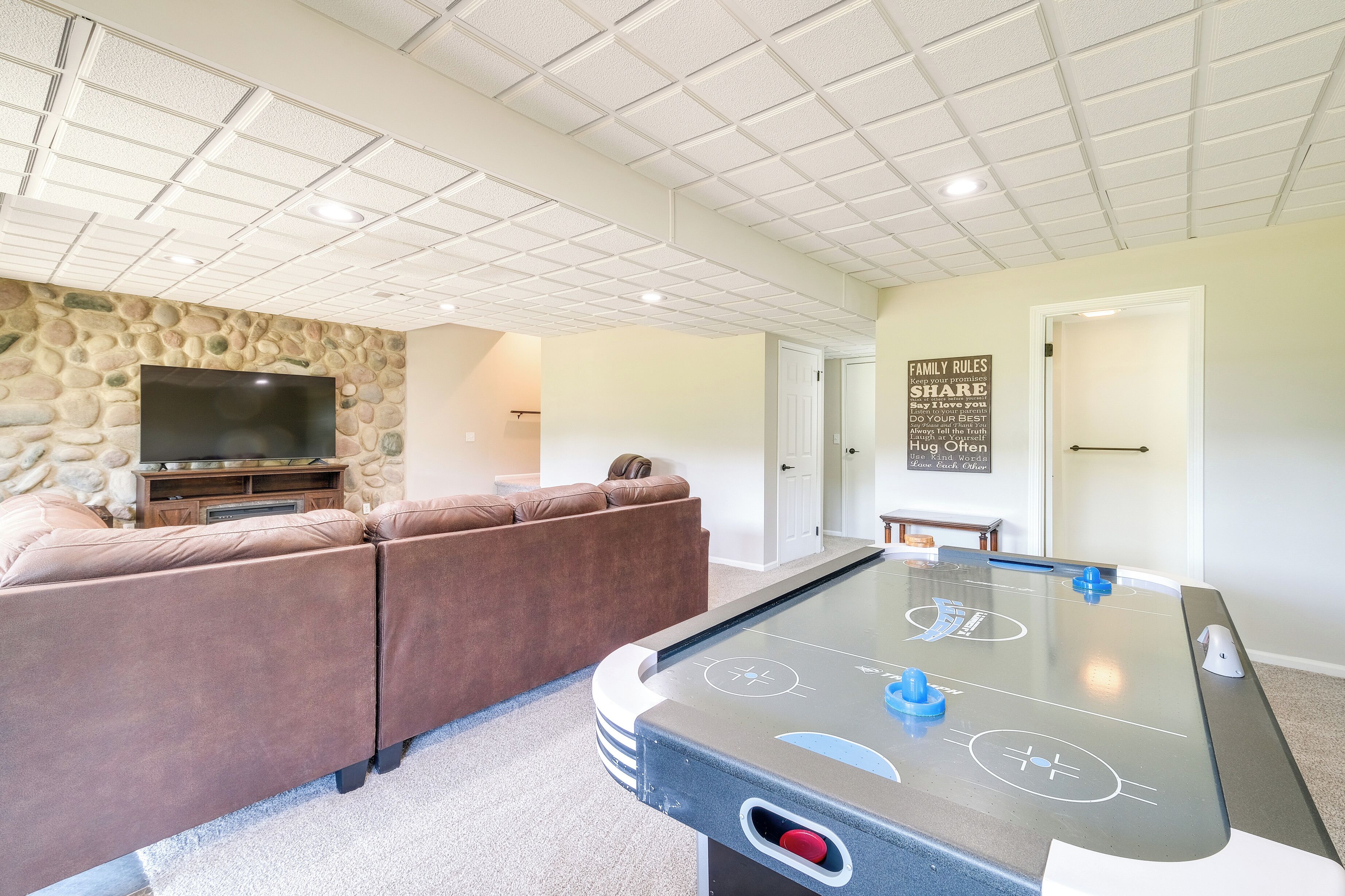 A living room with a stone wall, a flat-screen TV, a brown sectional sofa, and a foosball table.
