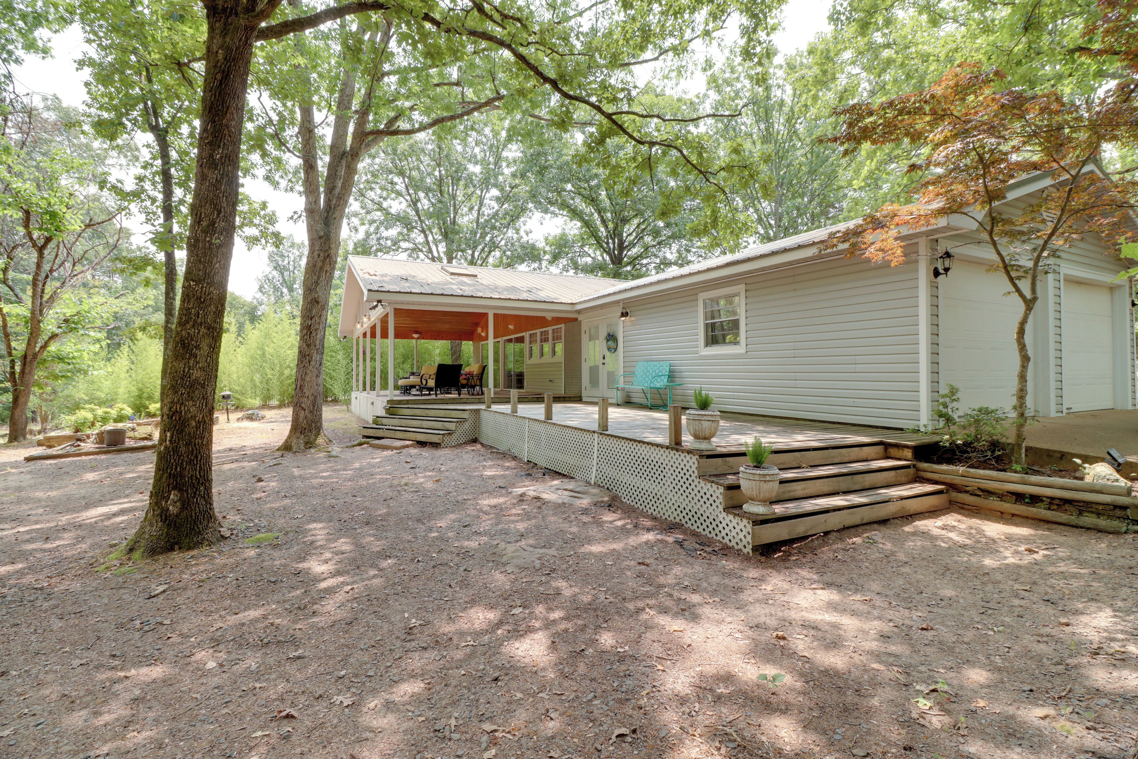 A rustic cabin with a covered porch, surrounded by trees and a dirt ground.